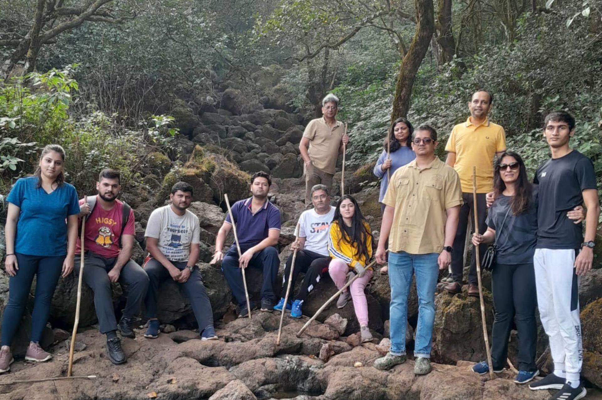 A group of guests at Ramsukh Resort enjoying a jungle trek, pausing at a rocky area surrounded by dense trees and foliage.